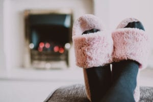 Person wearing fluffy pink house slippers in front of the fireplace.