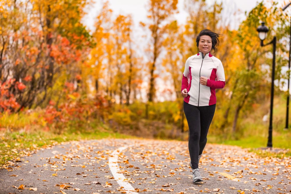 Middle aged female jogging outdoors in beautiful autumn city park in colorful fall foliage.